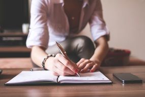 young woman writing on notebook, hands close up