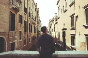 back view of young man on bridge looking at building, italy, venice