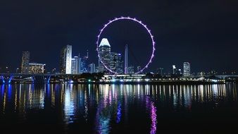 big ferris wheel in night cityscape with lights mirroring on water, singapore