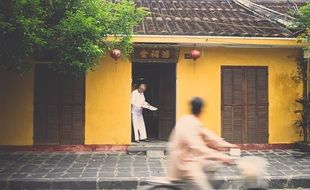 asian man reading paper in doors of yellow building