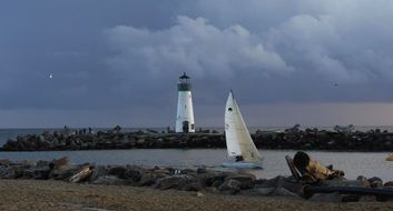 sailing boat on sea in view of lighthouse at cloudy evening