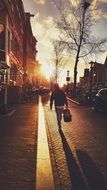 person with heavy bag walking on pavement in town at sunset