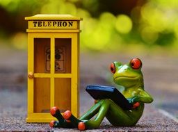 toy frog with laptop sits at phone booth