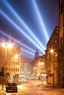 orange lamps on street and blue rays of light at dark sky above city