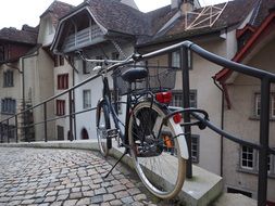 bicycle with basket stands at fence on cobblestone pavement in the beautiful old town, switzerland, aarau