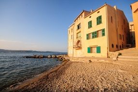 yellow house with green shutters on windows on beach at sea