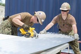 two women at work, construction workers cutting waved roofing sheet