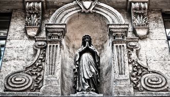 stone carving and praying woman sculpture on facade of old building