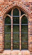 grated arched window in red brick wall