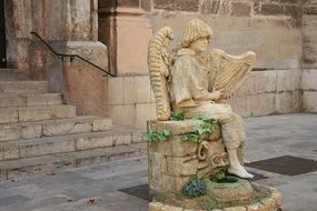 man with harp sits on antique fountain, sculpture