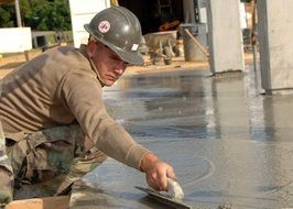 portrait of worker in hardhat smoothing cement with darby