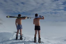 back view of two young men with skis on snowy mountain at sky