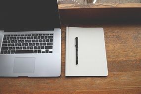 laptop and notebook with pen on wooden table