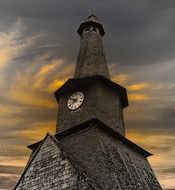 old church tower with clock and twisted spire at sunset sky