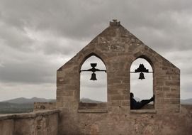 person sitting on old bell tower at cloudy sky, spain, mallorca