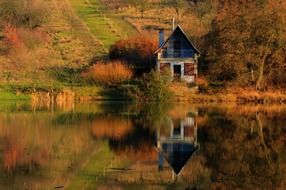 tranquil autumn landscape with cottage mirroring on lake