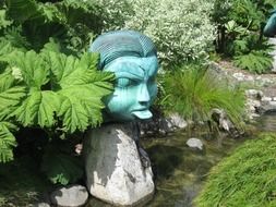 human head with long tongue, garden sculpture among plants