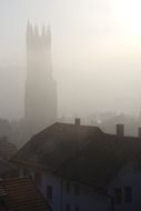 gothic tower in mist above tile roofs of old town, switzerland, fribourg