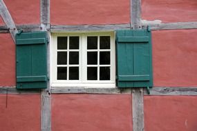 window with green shutters on the pink facade of a fachwerkhaus