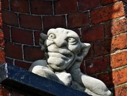 gargoyle, grey stone figure at red brick wall