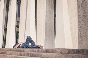 man in jeans lying on stone steps at facade