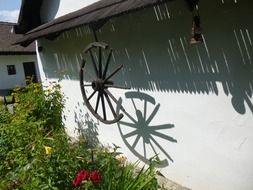 shadow of old wooden wheel on facade of village house with the plants