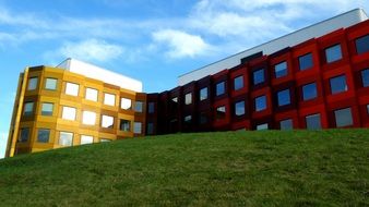 yellow and red intersecting buildings behind green hill