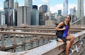 happy young girl sits on metal construction in view of city, usa, manhattan, nyc