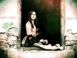 young pretty girl sits in doorway of old ruined house