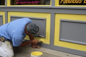 worker painting building wall with yellow paint