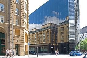 mirroring of old building on glass modern facade in city, uk, england, london