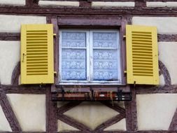 window with yellow shutters on facade of truss building, france