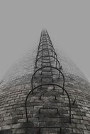bottom view of metal stairs on brick industrial chimney in fog
