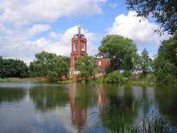 red church building at water, summer landscape, russia