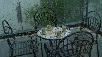 armchairs and round table with cups on balcony at rain