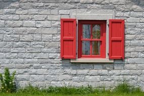 red wooden window with shutters on grey stone facade