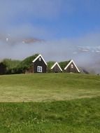 traditional torfhauses on green meadow at foggy mountain, scenic landscape, iceland