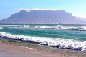 foamy sea waves splashing on beach in view of table mountain, south africa, cape town