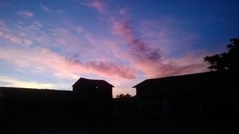 purple clouds in deep blue sky above dark silhouettes of country houses