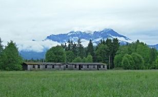 ruined wooden farm building on green meadow at snow capped mountains