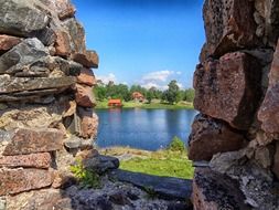 view of red houses on green coast through stone ruin, sweden