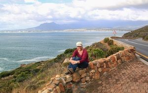 caucasian woman sits on stone fence at scenery coast, south africa, cape town