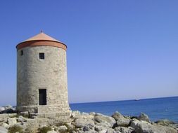 old flour mill on rocky coast at blue sea, greece, rhodes