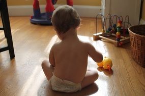 baby plays toys on floor, back view