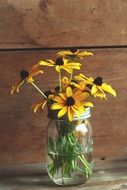 water glass jar yellow flowers wood backgraund