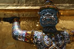 ornate metal demon figure at golden wall of temple, thailand