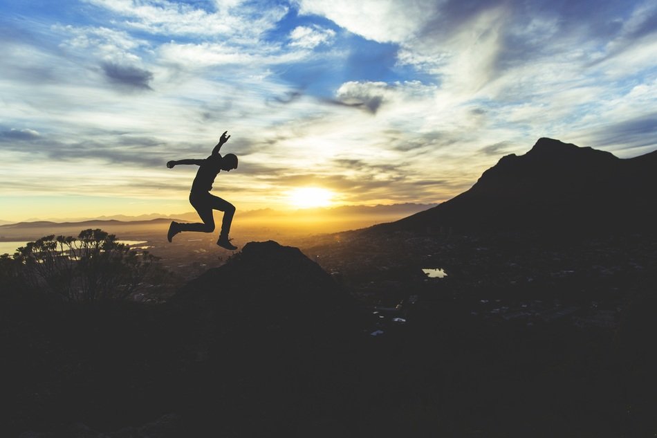young boy jumping on rocks, shilouette at beautiful sunset sky