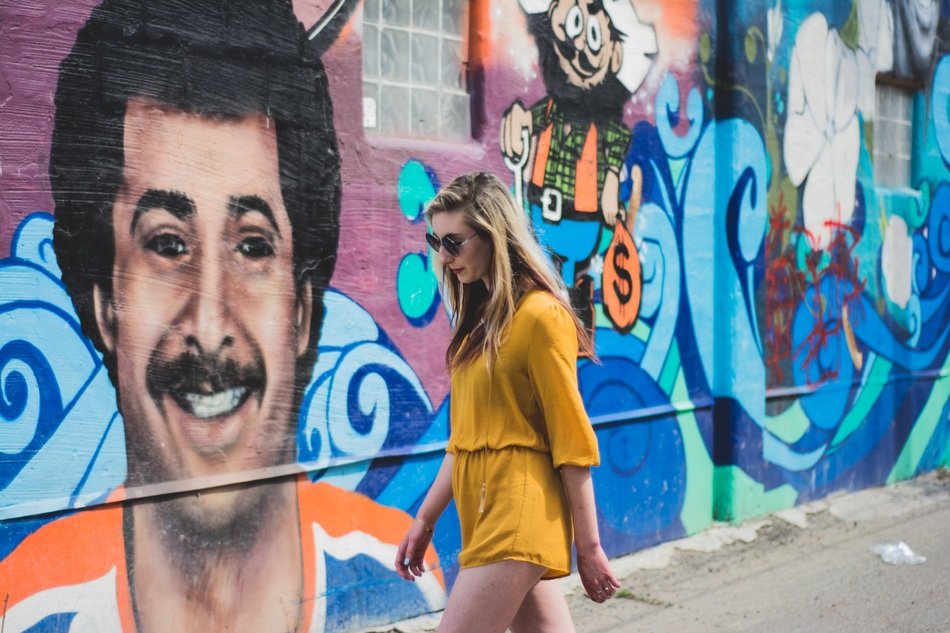 young woman walking on street with the wall with graffiti on background