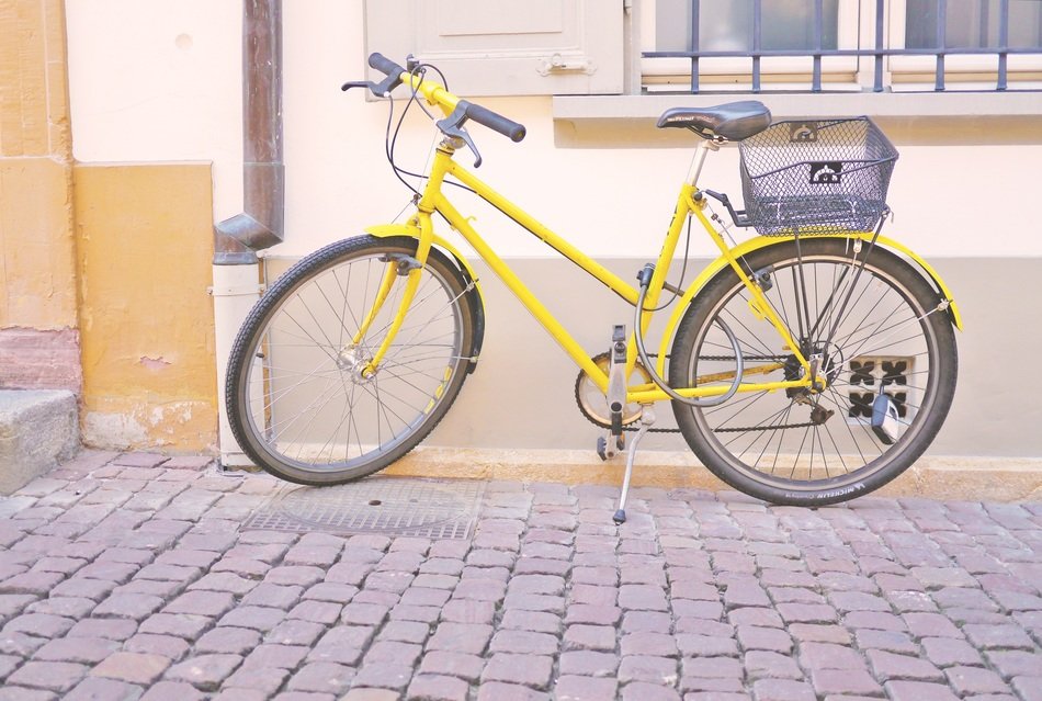 yellow bike with basket stands on pavement at facade