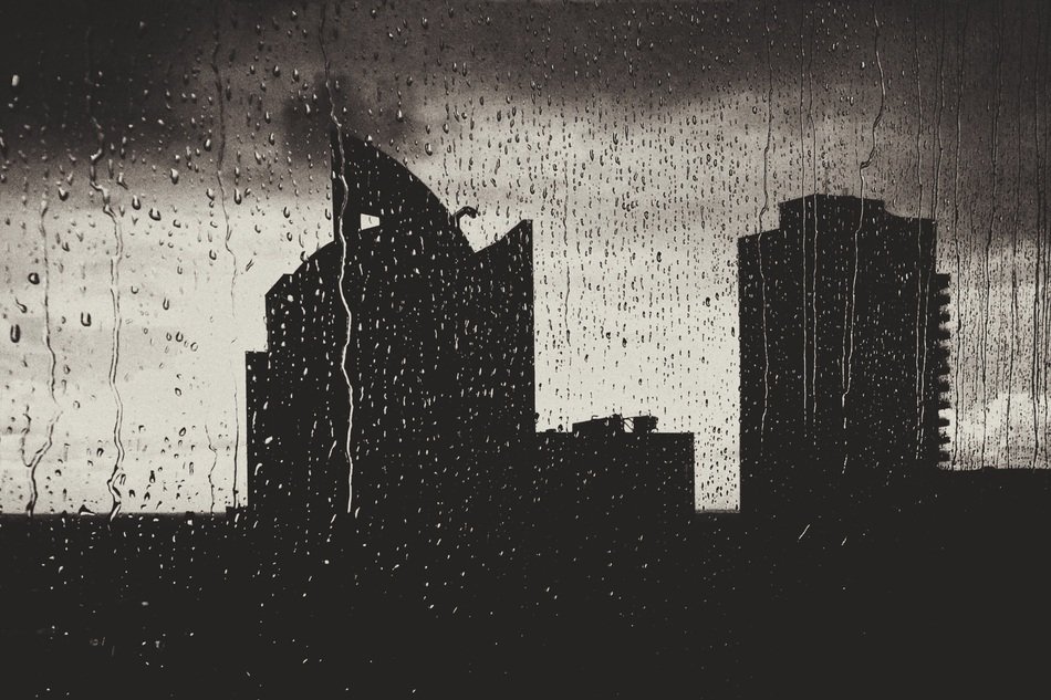 buildings at cloudy sky, view through wet window